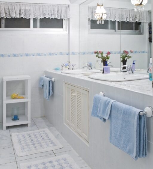 Bright bathroom with double sinks, blue towels, tiled counter, white cabinets, and potted flowers on the counter.