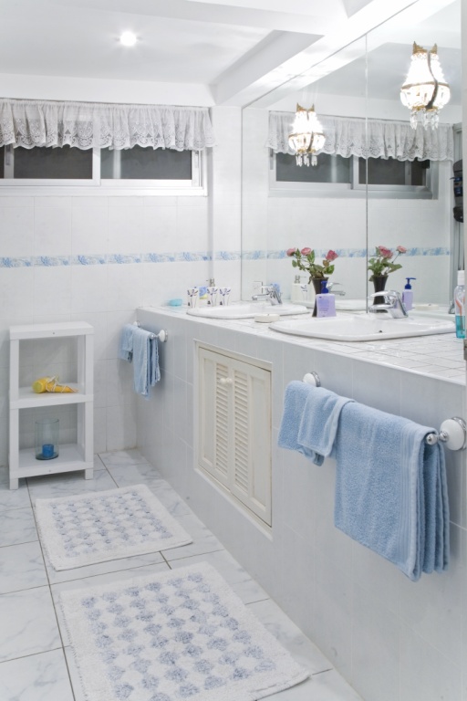 Bright bathroom with double sinks, blue towels, tiled counter, white cabinets, and potted flowers on the counter.