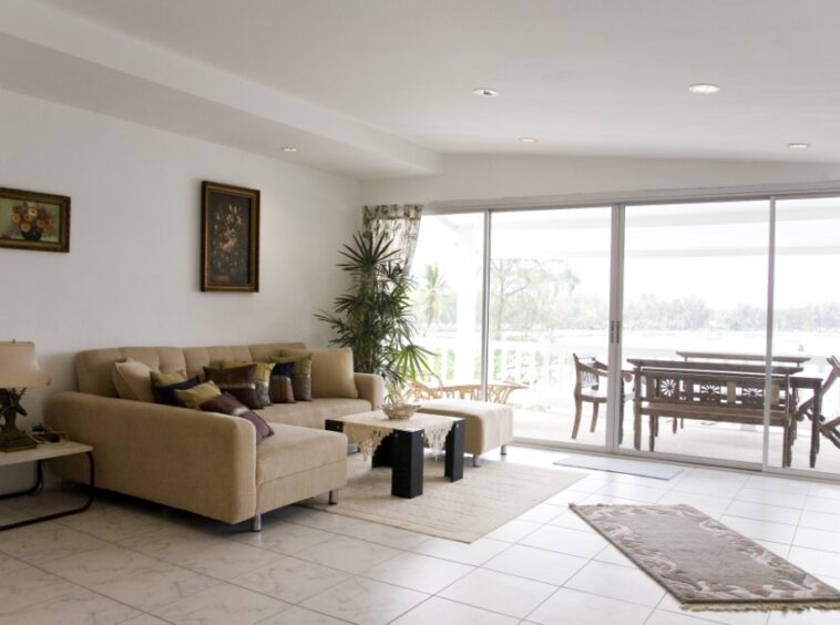 Bright living room with a beige sectional sofa, decorative pillows, and glass sliding doors to a covered balcony with an outdoor dining set.