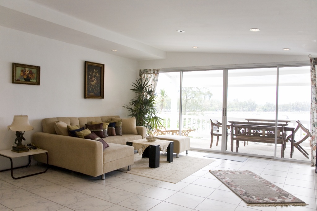 Bright living room with a beige sectional sofa, decorative pillows, and glass sliding doors to a covered balcony with an outdoor dining set.