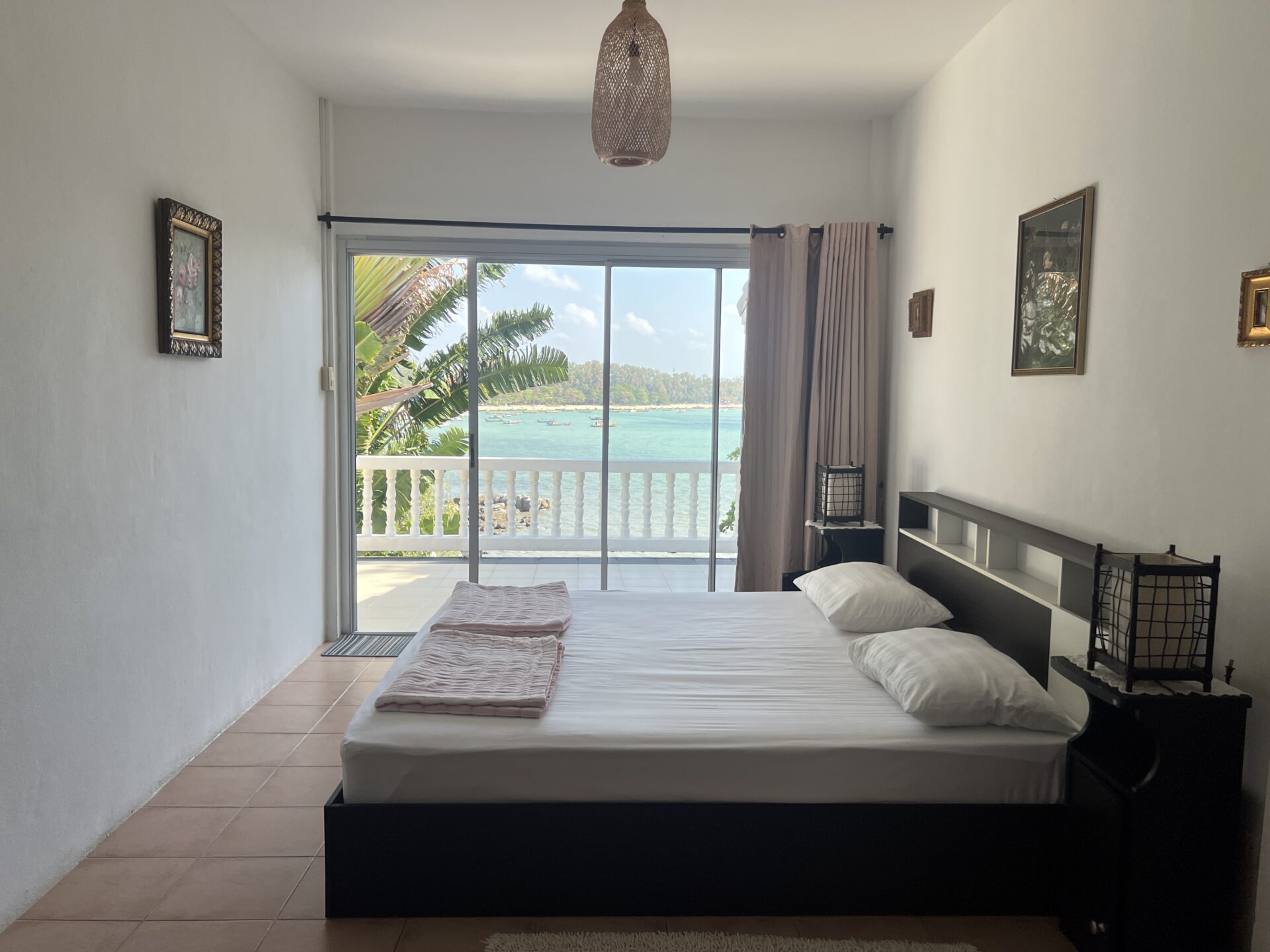 Bedroom with a large sliding glass door to a balcony overlooking the ocean; bed in foreground with pink throws and white pillows.
