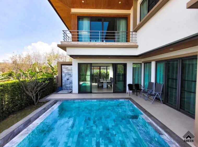 Modern two-story home with a rectangular pool, glass doors, and outdoor seating on a sunny backyard patio