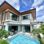 Modern two-story house with wooden overhangs, glass doors, and a rectangular pool in the courtyard, under a bright sky.
