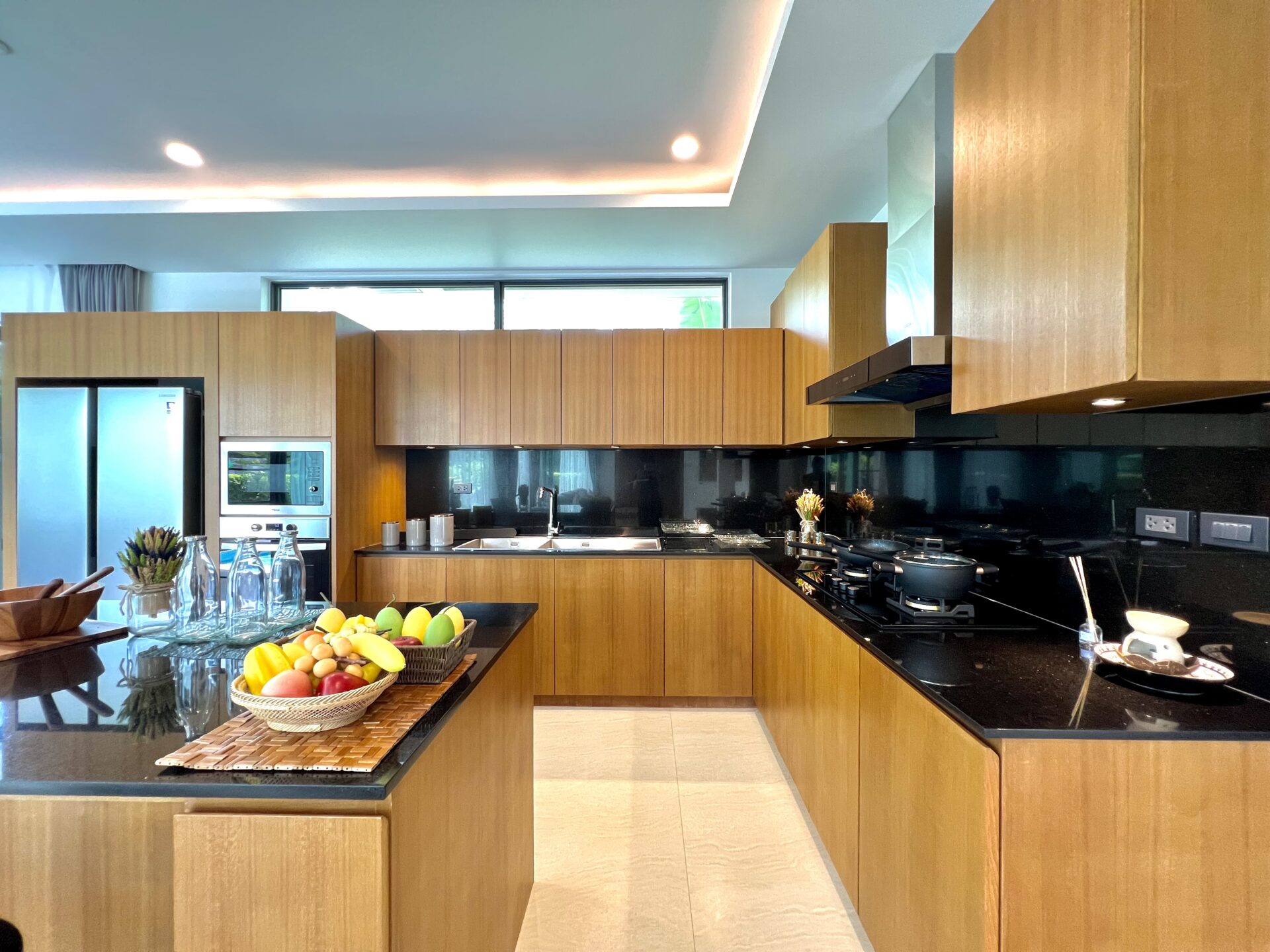 Modern kitchen with wooden cabinets, black countertops, and a central island displaying fruit and glass bottles