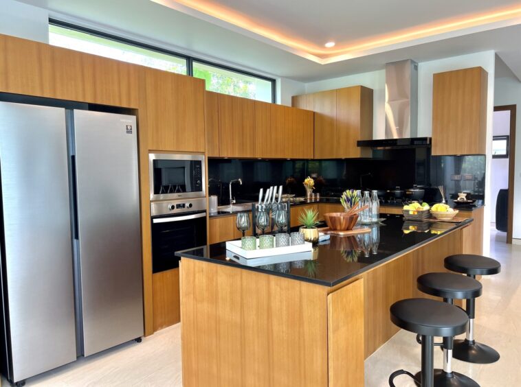 Modern kitchen with tall wooden cabinets, stainless fridge, and a dark granite island with bar stools.