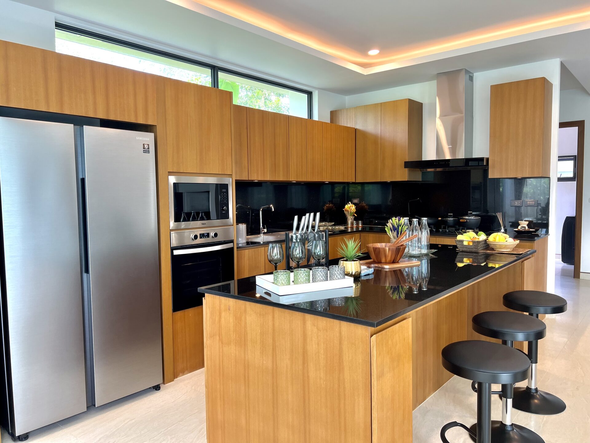 Modern kitchen with tall wooden cabinets, stainless fridge, and a dark granite island with bar stools.