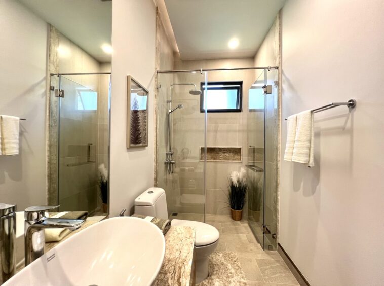Modern bathroom with a glass-enclosed shower, beige tile walls, and a stone countertop sink in the foreground.