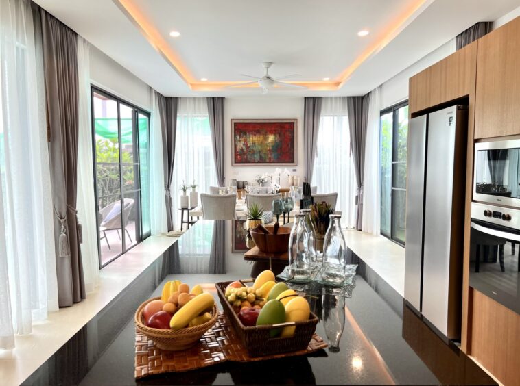 Contemporary kitchen and dining area with a glossy black island, fruit baskets, and stainless steel appliances under warm ceiling lighting.