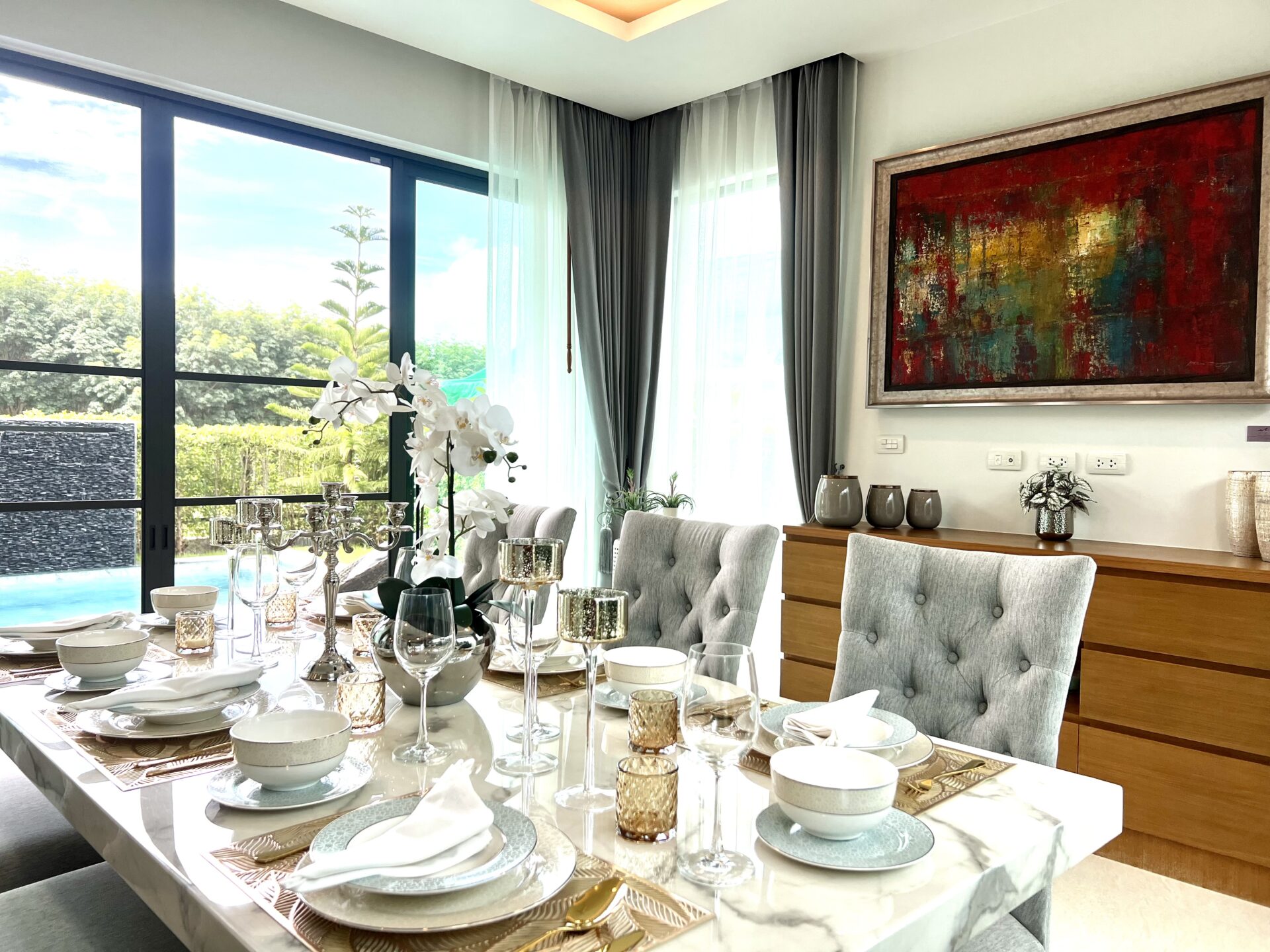 Elegant dining room with a marble table set for a formal meal, gray upholstered chairs, and a large abstract painting on the wall