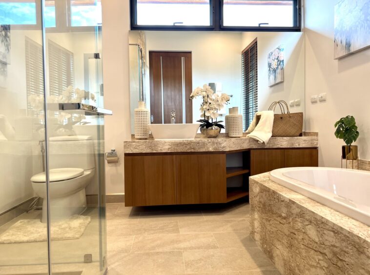 Modern bathroom with twin sinks on a marble countertop, and a glass shower enclosure on the left.