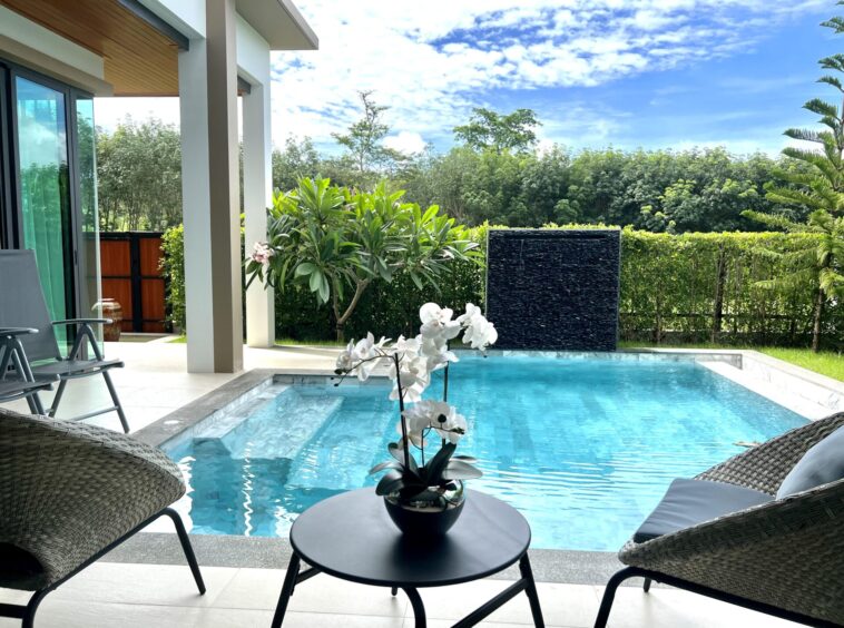 Poolside patio with wicker lounge chairs, a round table with an orchid centerpiece, and a bright blue pool water edge.