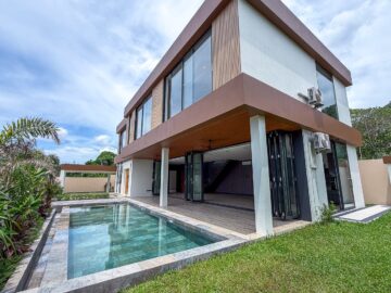 Contemporary two-story house with large glass windows and a rectangular in-ground pool in the backyard under a blue sky.