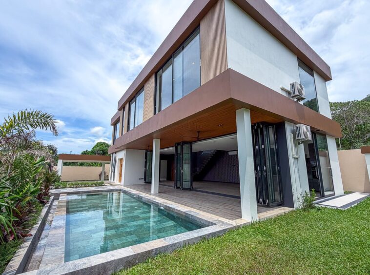 Contemporary two-story house with large glass windows and a rectangular in-ground pool in the backyard under a blue sky.