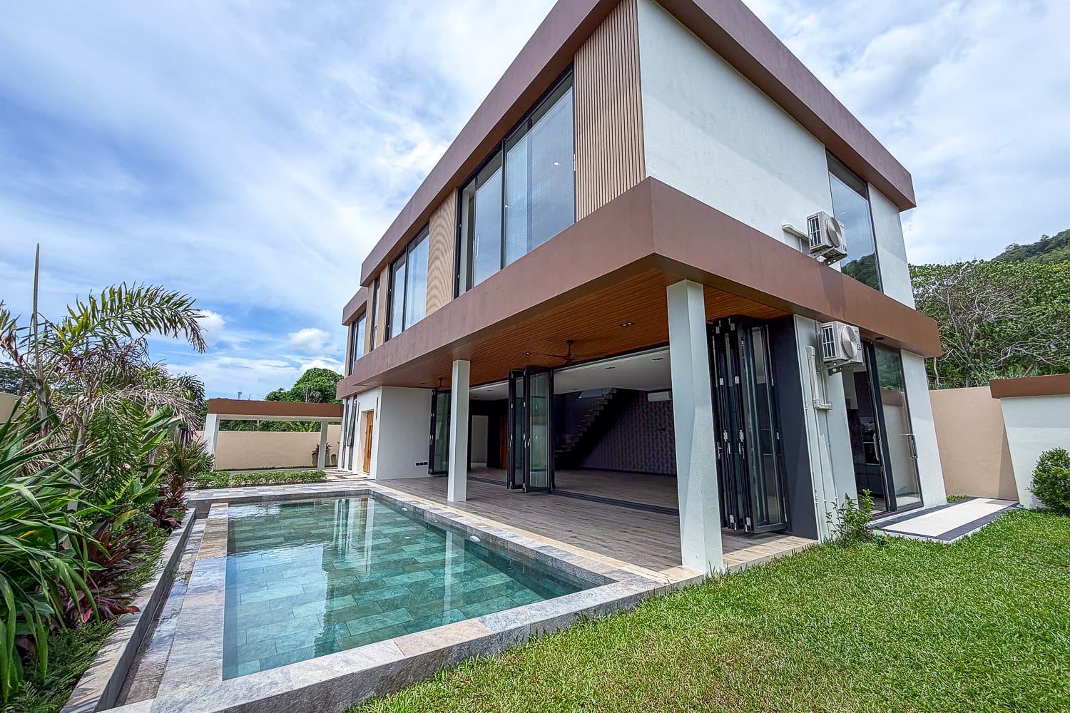 Contemporary two-story house with large glass windows and a rectangular in-ground pool in the backyard under a blue sky.