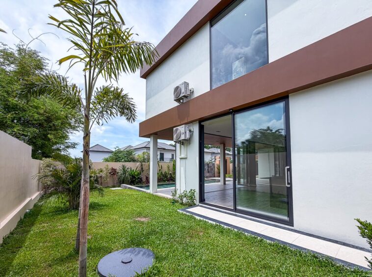 Modern two-story house with large glass sliding doors leading to a green backyard, a tall palm tree in the lawn, and exterior AC units mounted on the wall.