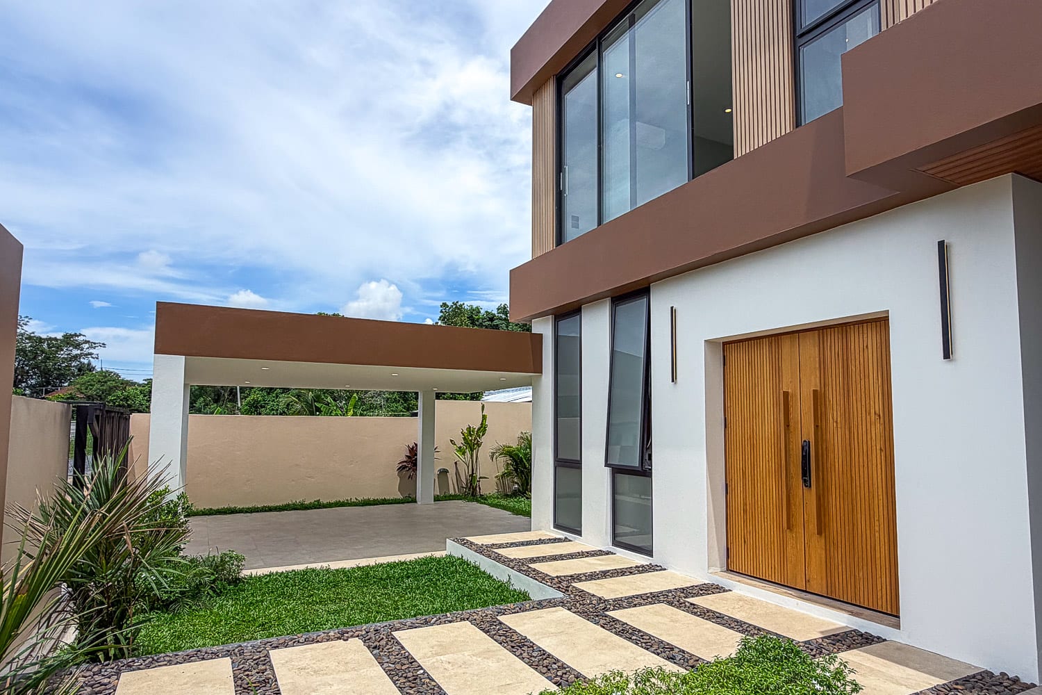 Modern two-story home with white walls, large glass windows, and a tall wooden front door under a brown overhang.