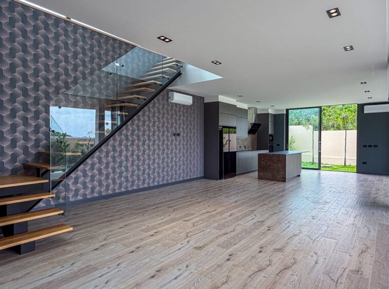Open-plan living area with a glass-railed staircase, geometric-pattern wall, and a modern kitchen with island.
