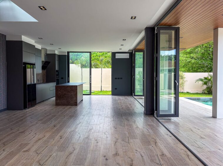 Open-plan kitchen with gray cabinets, central brown island, and large glass doors opening to a backyard and pool.