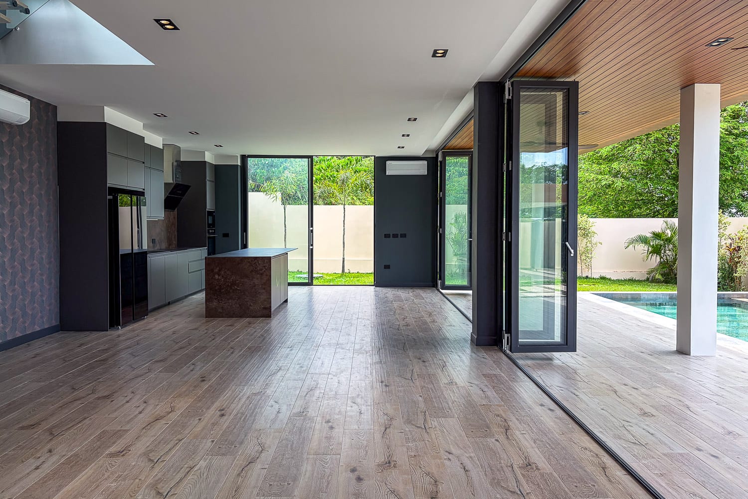 Open-plan kitchen with gray cabinets, central brown island, and large glass doors opening to a backyard and pool.