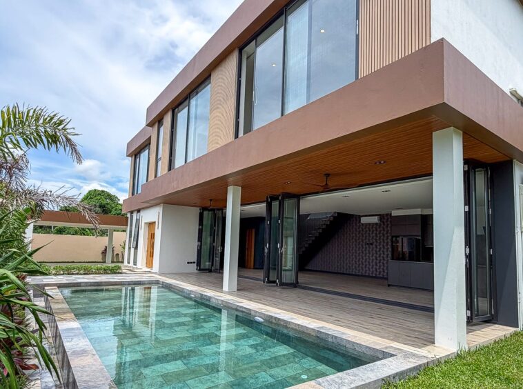 Modern two‑story home with large glass walls, timber accents, and a rectangular pool on the patio area.