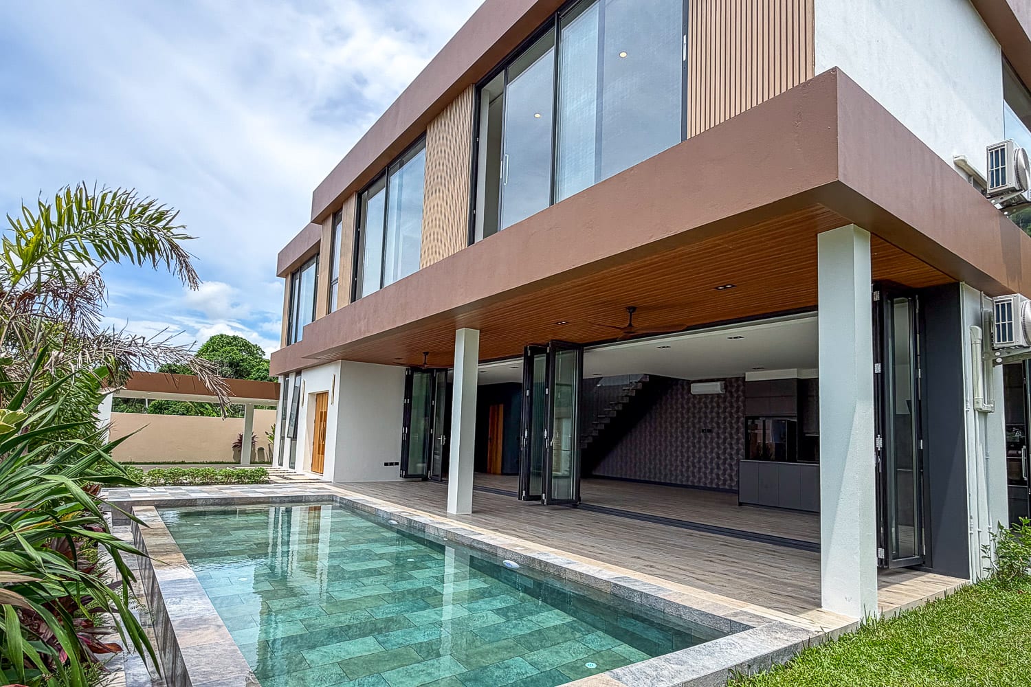 Modern two‑story home with large glass walls, timber accents, and a rectangular pool on the patio area.