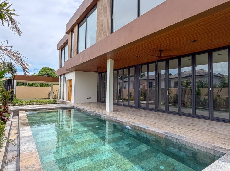 Modern two-story house with large glass doors along a covered patio and a rectangular turquoise swimming pool.