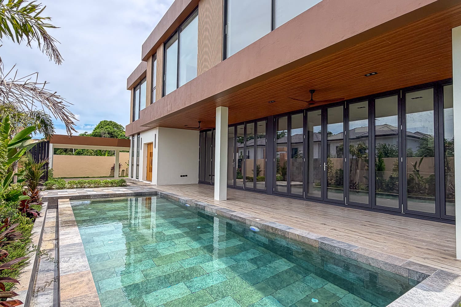 Modern two-story house with large glass doors along a covered patio and a rectangular turquoise swimming pool.