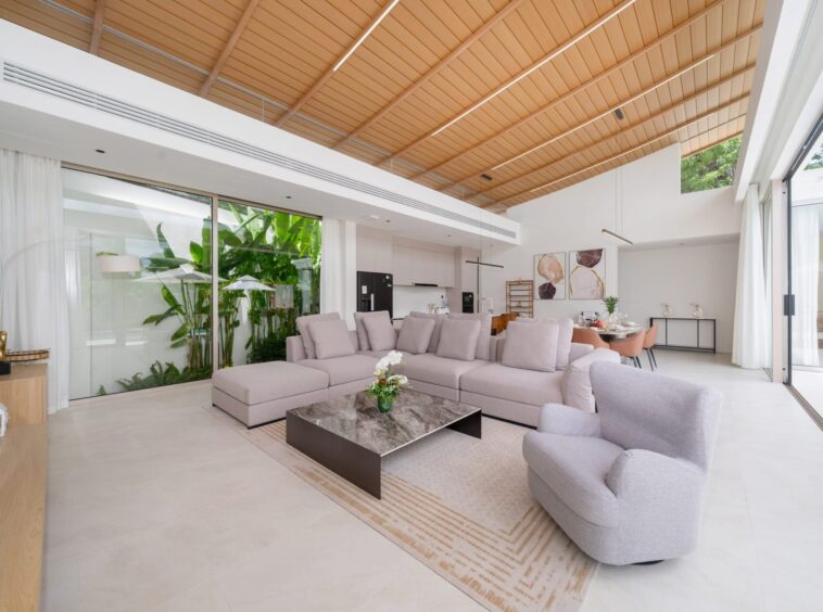 Bright open-plan living room with a gray sectional sofa, marble coffee table, and glass doors opening to a garden view.