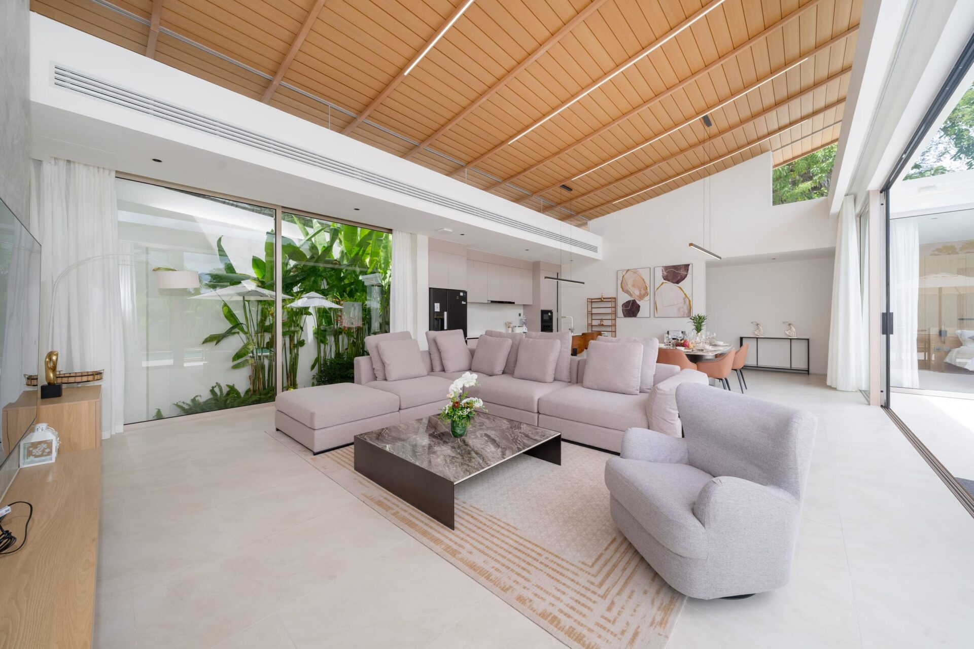 Bright open-plan living room with a gray sectional sofa, marble coffee table, and glass doors opening to a garden view.