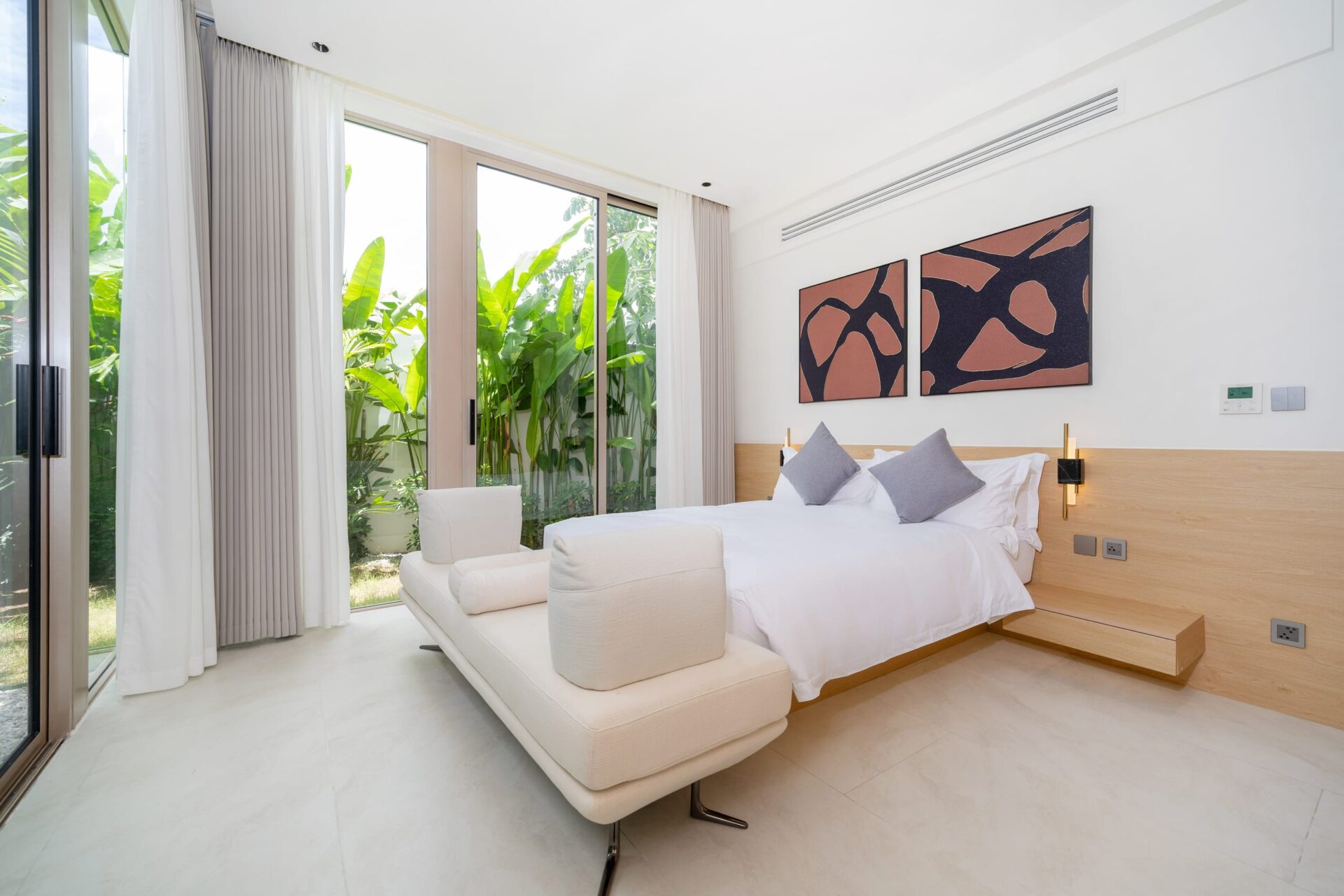 Modern bedroom with floor-to-ceiling glass doors opening to greenery, white bedding, and two abstract art panels above the bed.
