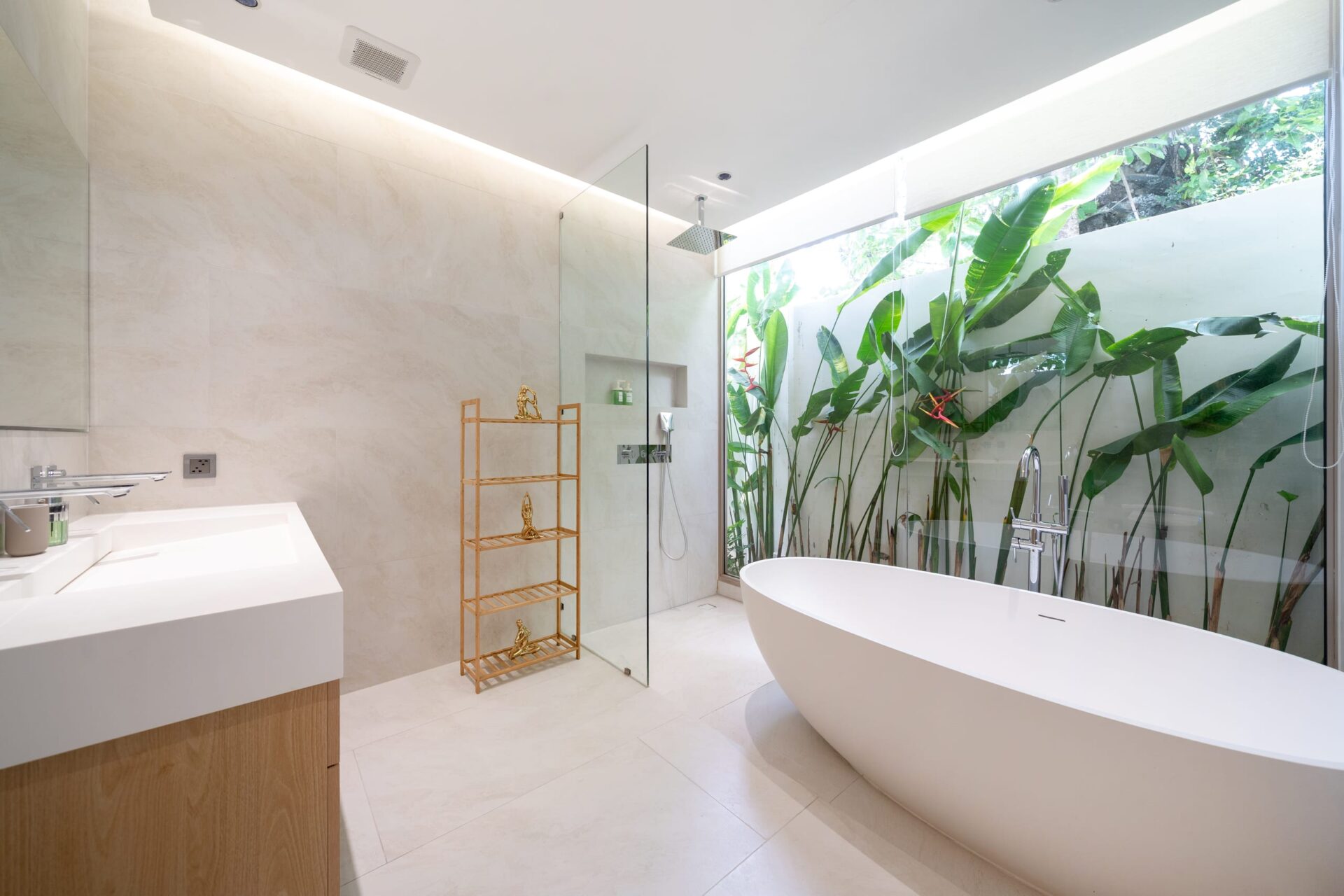 Bright, modern bathroom with a freestanding white tub, glass-enclosed shower, and a large glass wall overlooking tropical plants.