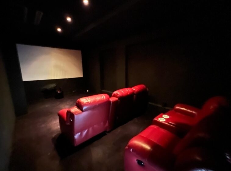 Dark home theater with red leather recliners facing a large screen on the left in low lighting