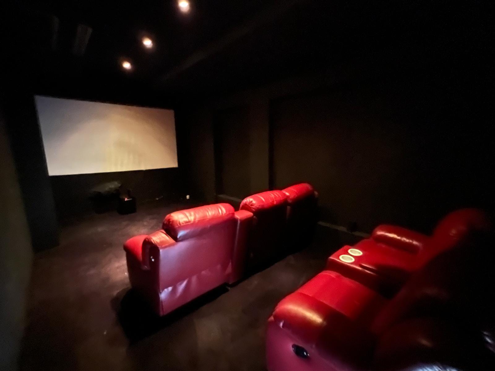 Dark home theater with red leather recliners facing a large screen on the left in low lighting