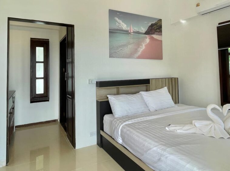 Hotel room with a large bed, white linens, and towel swans at the foot; wall art of a beach sea scene above the headboard.