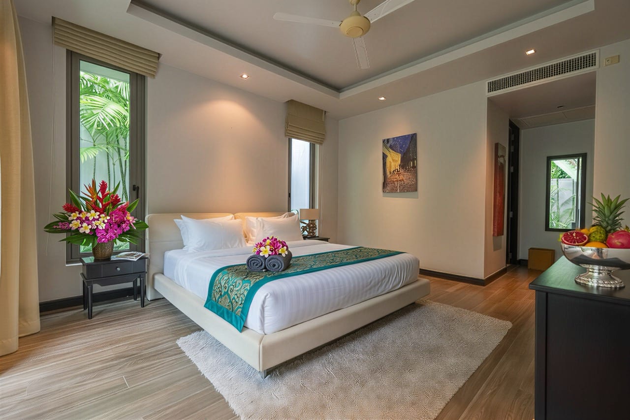 Luxurious hotel bedroom with a white platform bed, teal runner, and fresh flower arrangements on each side table; tropical plants outside the windows.