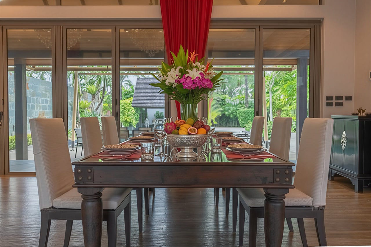 Elegant dining room with a dark wood table set for eight, white upholstered chairs, and a centerpiece of fruit and tropical flowers.