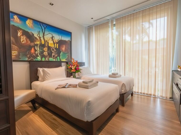 Hotel room with two single beds, white linens, and a colorful mural above the headboards; flowers between beds.