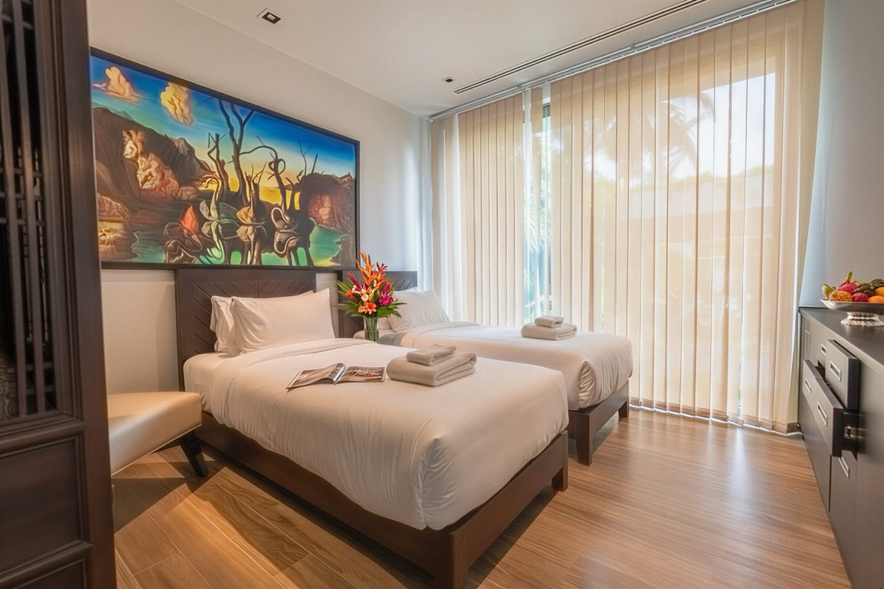 Hotel room with two single beds, white linens, and a colorful mural above the headboards; flowers between beds.