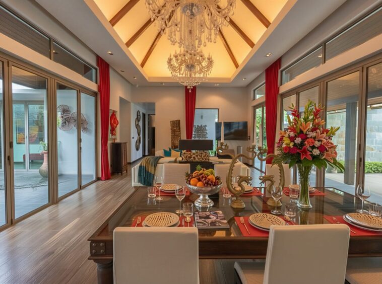 Elegant dining room and living area with chandelier, glass table set for six and a flower centerpiece in the center.