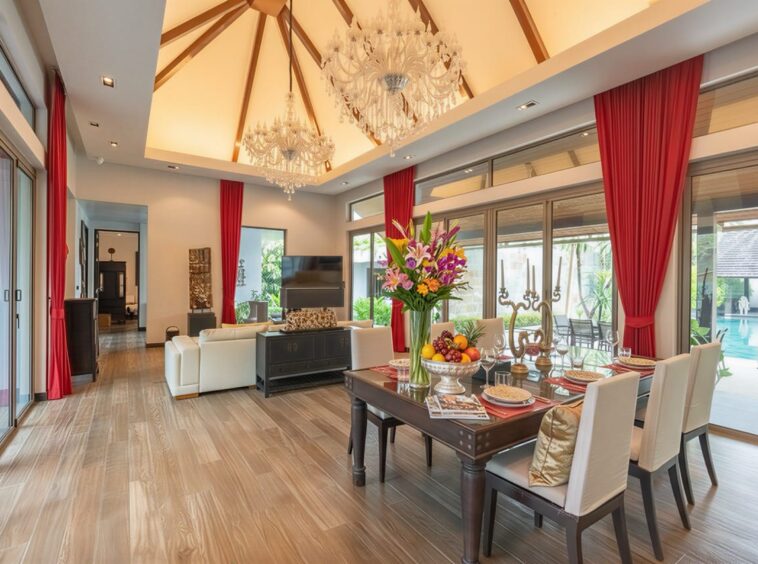 Luxurious open-concept living and dining room with a chandelier, red drapes, and a dining table set by glass doors to a pool oasis for eight people.