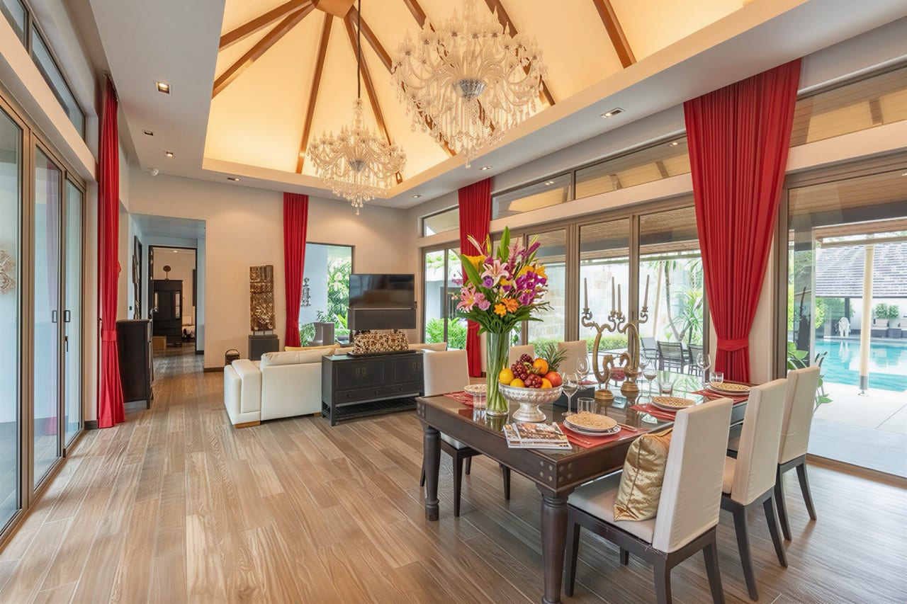 Luxurious open-concept living and dining room with a chandelier, red drapes, and a dining table set by glass doors to a pool oasis for eight people.