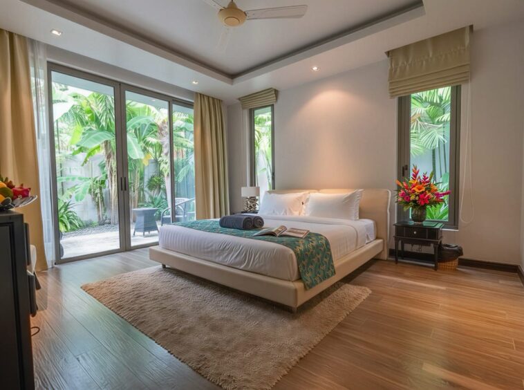 Spacious hotel bedroom with a king bed, white linens, teal throw, and sliding glass doors to a tropical garden patio.