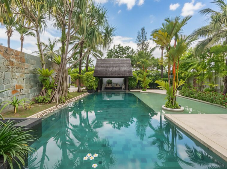 Poolside tropical garden with palm trees and a thatched pavilion reflecting in turquoise pool.