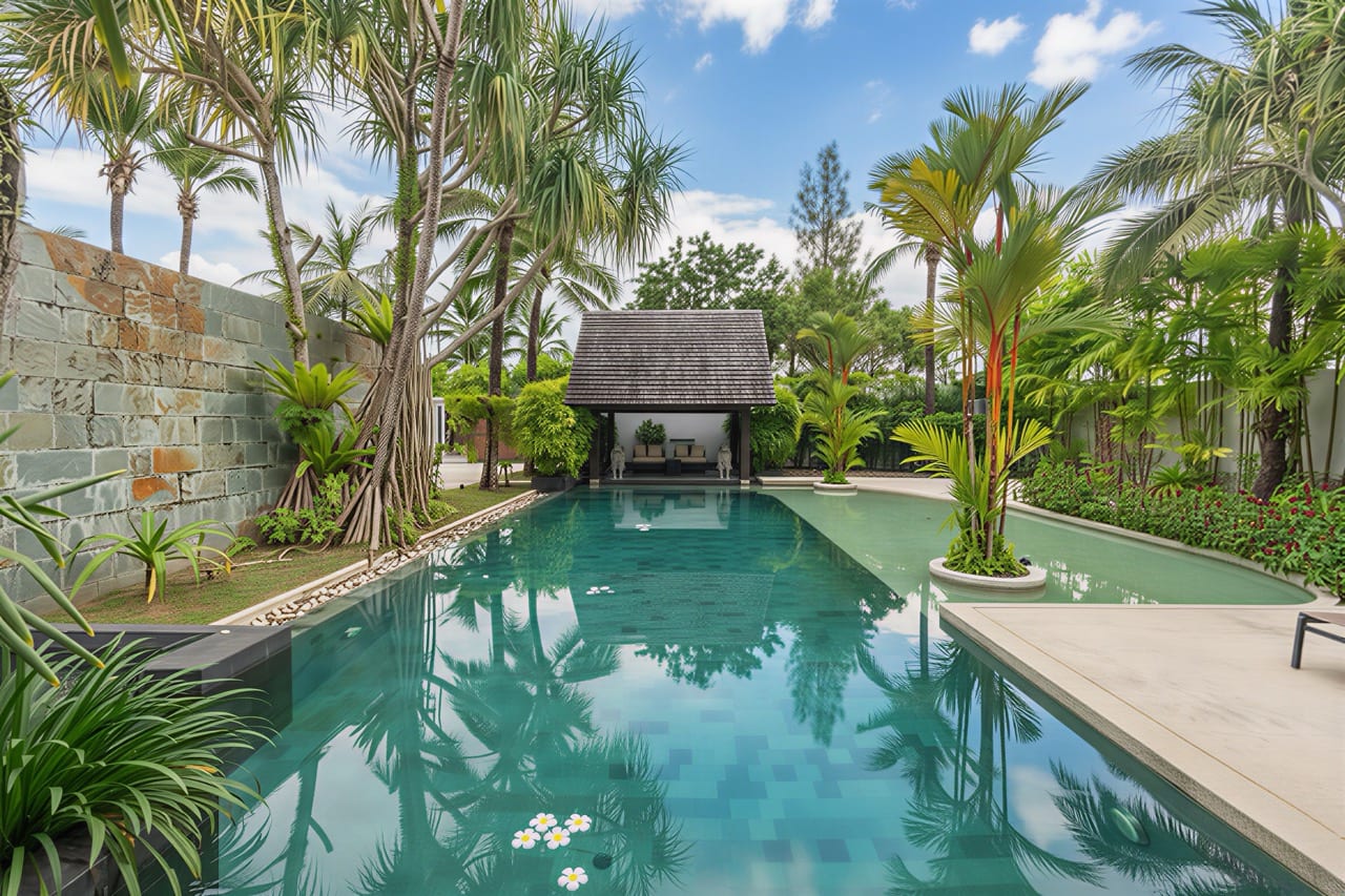 Poolside tropical garden with palm trees and a thatched pavilion reflecting in turquoise pool.