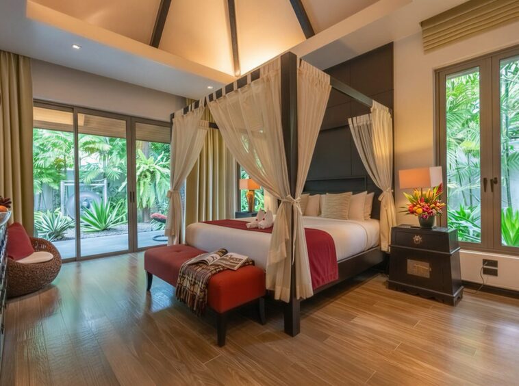 Luxurious hotel bedroom with a four-poster bed, sheer drapes, and tropical greenery outside the sliding doors.