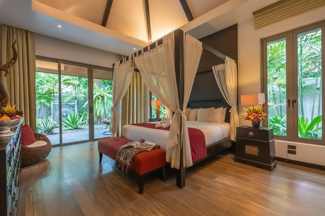 Luxurious hotel bedroom with a four-poster bed, sheer drapes, and tropical greenery outside the sliding doors.