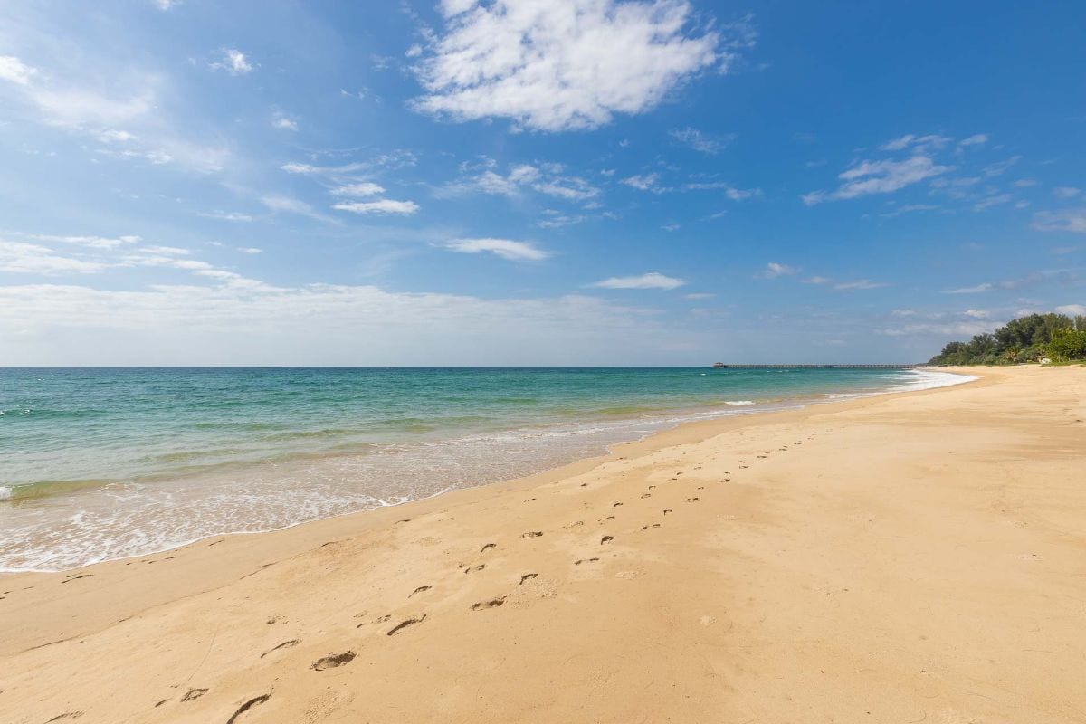 Sunny beach with turquoise water, blue sky, and footprints in the wet sand leading toward the water.