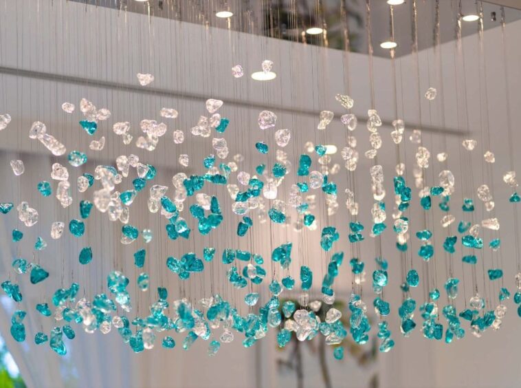 Installation of turquoise and clear glass beads hanging from wires in a bright indoor space.