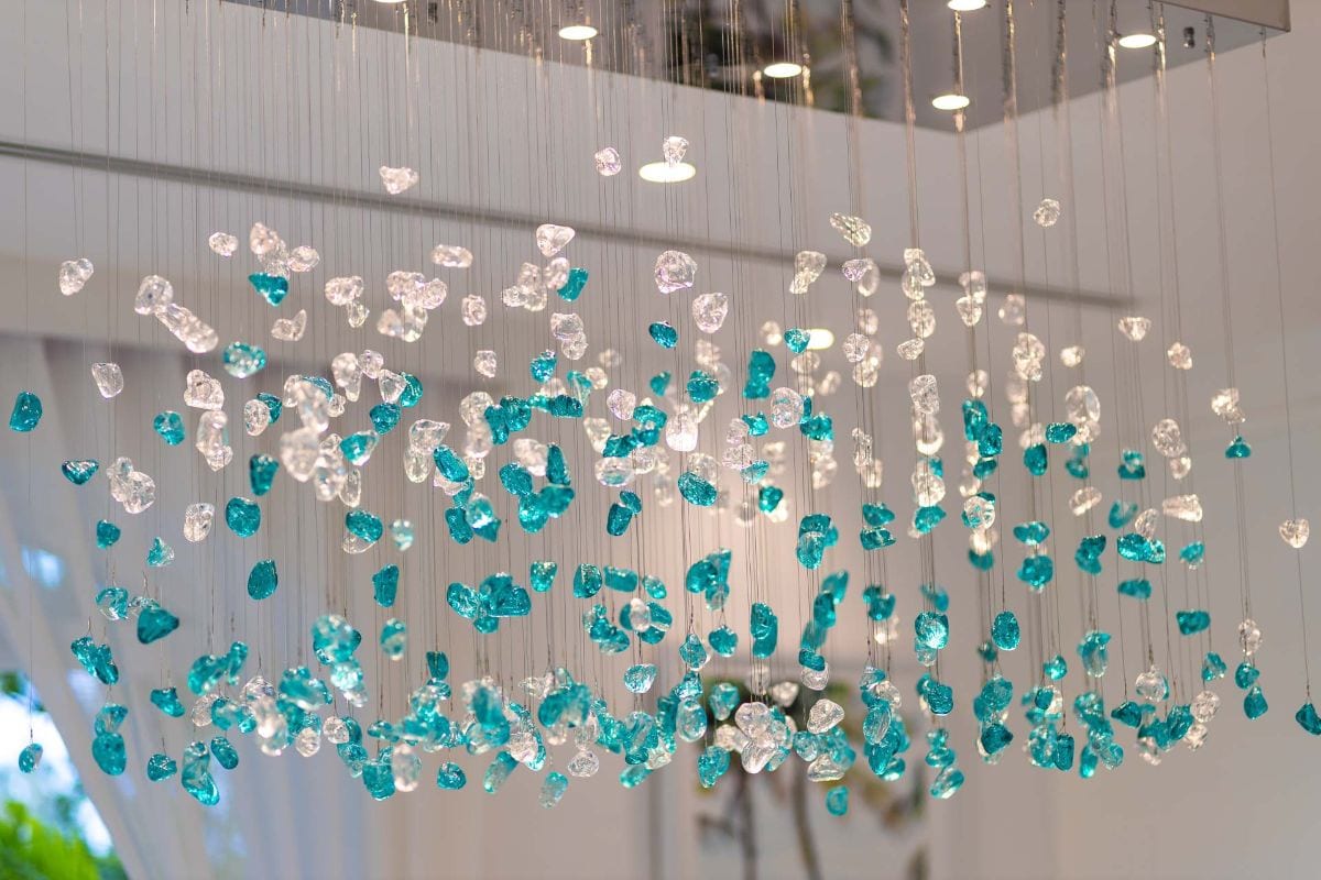 Installation of turquoise and clear glass beads hanging from wires in a bright indoor space.