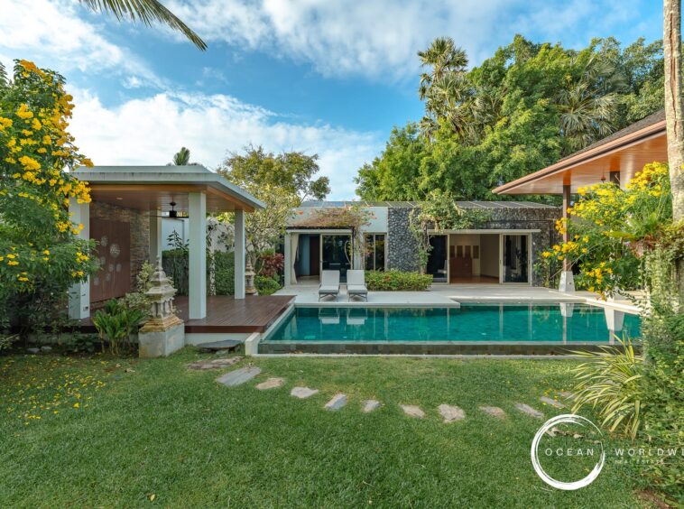 Luxurious villa with a rectangular pool, lounge chairs, and tropical landscaping under a bright blue sky at a resort-style backyard.
